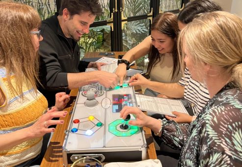 A group of participants working together on a Team Synergy retro gaming console, solving puzzles and collaborating during a team building activity.