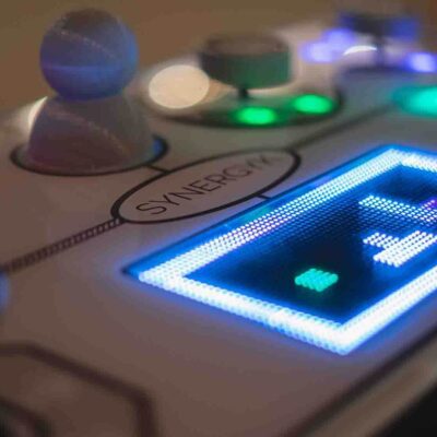 Close-up of the illuminated Team Synergy retro gaming console showcasing bright LED displays, joysticks, and sliders for a team building challenge. thumbnail