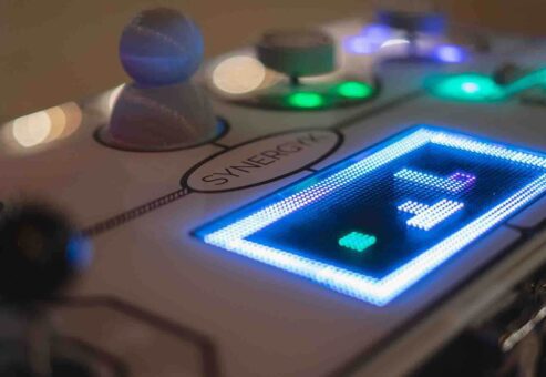 Close-up of the illuminated Team Synergy retro gaming console showcasing bright LED displays, joysticks, and sliders for a team building challenge.