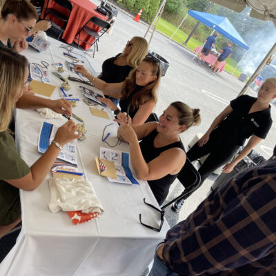 Group of people sitting at a table outdoors working on a team building activity with various materials during a corporate charitable activity. thumbnail