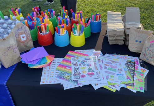 Table set up with colorful markers, stickers, and brown paper bags ready to be decorated during a corporate charitable team building event.