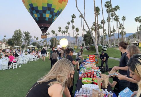 Outdoor corporate charitable team building event with a colorful hot air balloon in the background and participants decorating kits at a table filled with supplies.