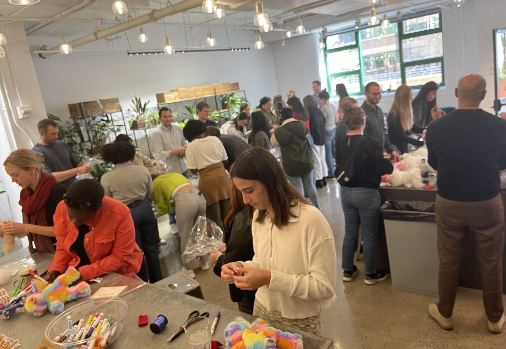 A large group of people working together to assemble donation kits during a busy corporate charitable team building event called The Donation Station.