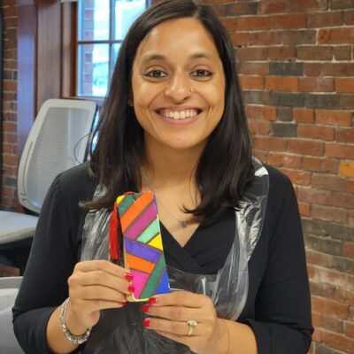 Smiling participant proudly displays a colorful, hand-painted bookmark during a team building activity for Little Team Library. The event encourages collaboration and creativity as teams build and decorate Little Free Library kits, sharing stories and literary inspirations to promote community literacy. thumbnail