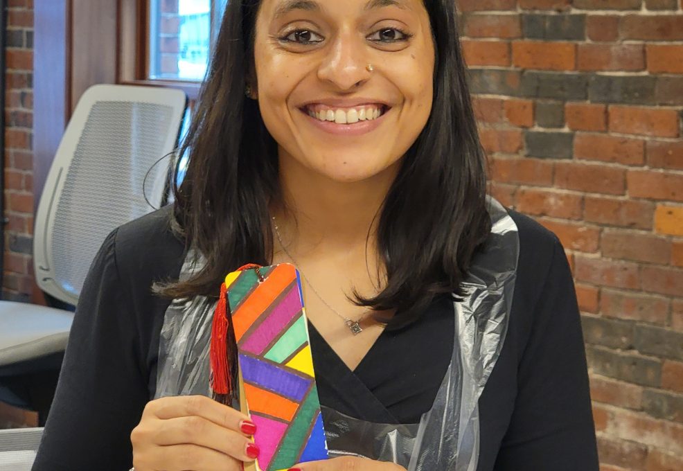 Smiling participant proudly displays a colorful, hand-painted bookmark during a team building activity for Little Team Library. The event encourages collaboration and creativity as teams build and decorate Little Free Library kits, sharing stories and literary inspirations to promote community literacy.