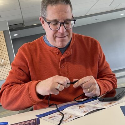 A man in an orange sweater is focused on connecting a cable while sitting at a table with documents and a pen. thumbnail