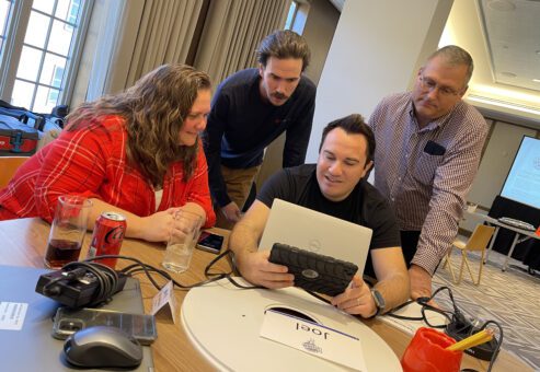 A group of four team members are looking at a tablet during the Wheels Around the World team building event.