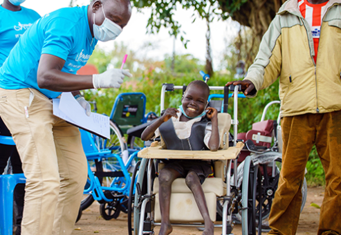 A smiling child in a wheelchair, sponsored by the Wheels Around the World team building event, receives care and attention from team members.