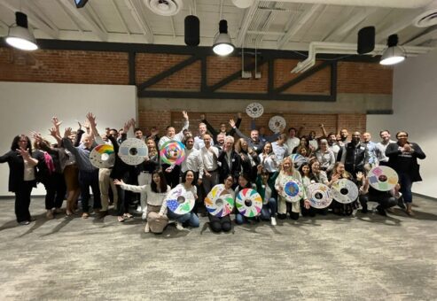 A large group of participants proudly display their decorated wheel safety covers during the Wheels Around the World team building event, celebrating their contribution to providing wheelchairs for individuals in need.