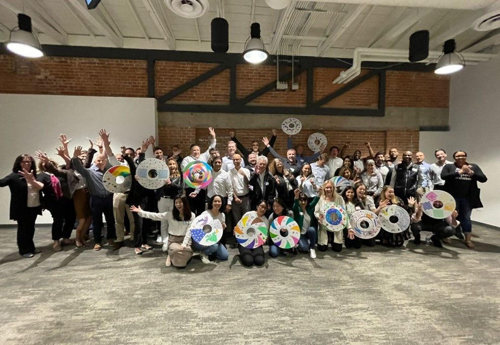 A large group of participants proudly display their decorated wheel safety covers during the Wheels Around the World team building event, celebrating their contribution to providing wheelchairs for individuals in need.