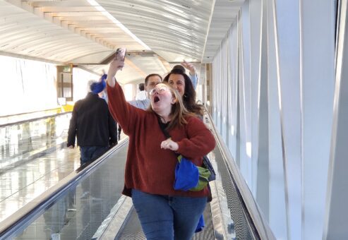 A group of participants on a moving walkway during a team building event, with one person enthusiastically taking a selfie.