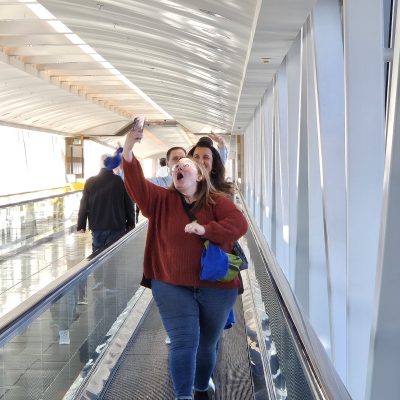 A group of participants on a moving walkway during a team building event, with one person enthusiastically taking a selfie. thumbnail