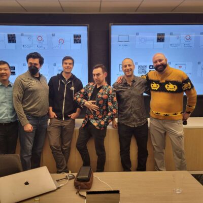 Team members look at their watches, adding a playful sense of urgency during the Monster Mash Dash scavenger hunt, surrounded by Halloween-themed decorations. thumbnail