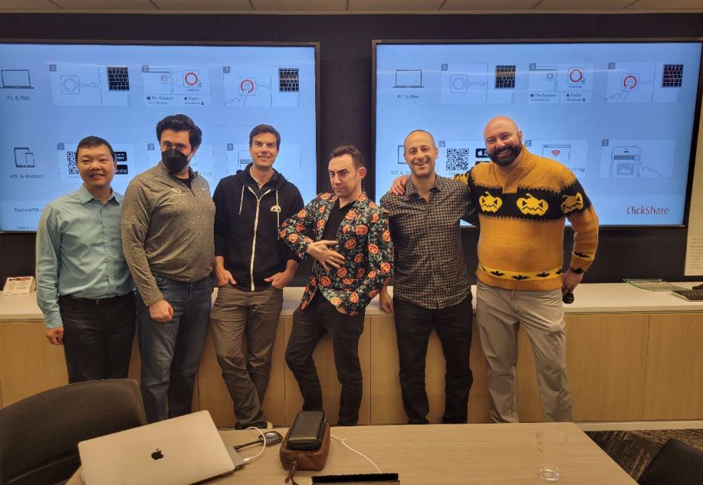 Team members look at their watches, adding a playful sense of urgency during the Monster Mash Dash scavenger hunt, surrounded by Halloween-themed decorations.