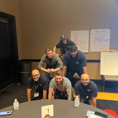 A group of participants in a team building event form a human pyramid indoors, smiling and working together. thumbnail