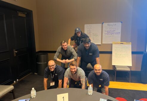 A group of participants in a team building event form a human pyramid indoors, smiling and working together.