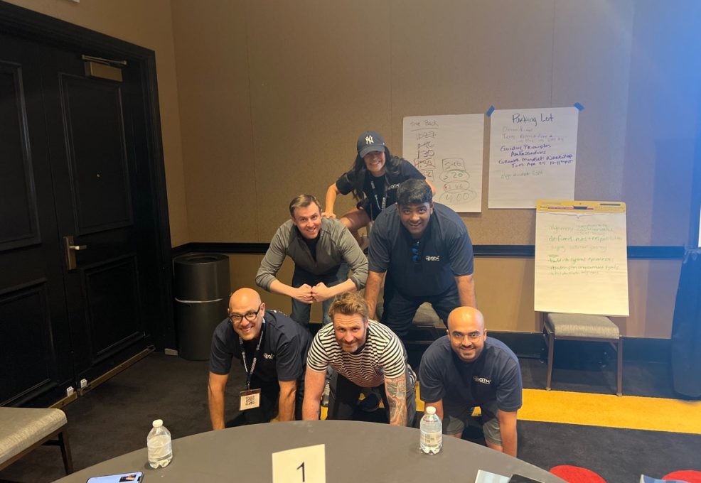 A group of participants in a team building event form a human pyramid indoors, smiling and working together.