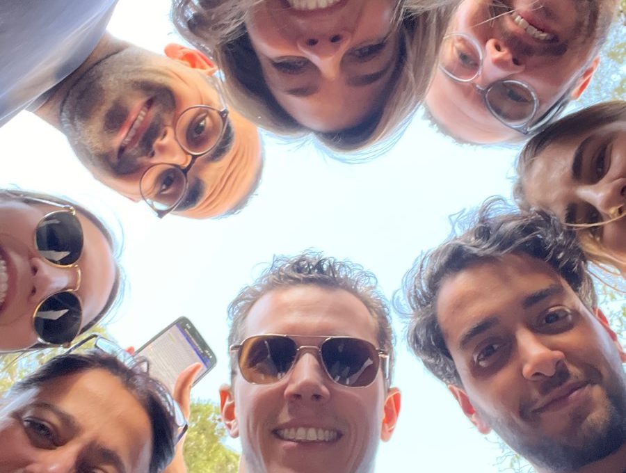 A group of smiling team members huddled in a circle, looking down at the camera during a fun and engaging outdoor team building activity.