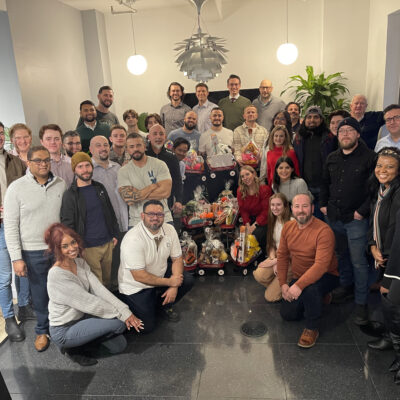 Team posing with holiday gift baskets, celebrating together during a festive team building event. thumbnail