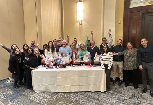 Team celebrating after completing holiday wagons filled with gifts for donation during a festive team building event.