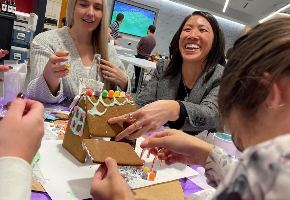 Team members enjoy decorating a gingerbread house during a festive team building activity at the holiday event.