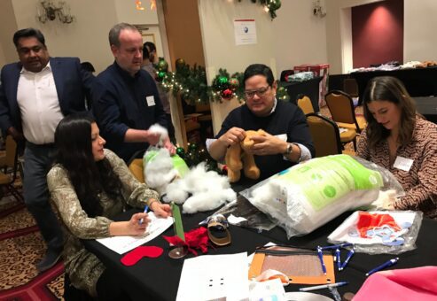 Team members collaborate to stuff teddy bears during a holiday team building activity focused on creativity and giving back.