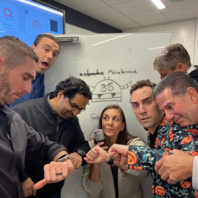 Team members gather in front of a screen after completing the Monster Mash Dash scavenger hunt, celebrating their Halloween-themed team building event. thumbnail