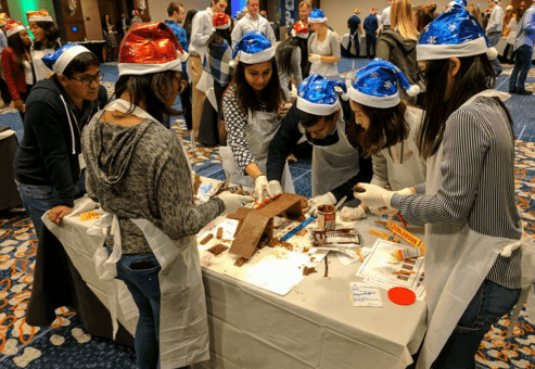 Team members wearing festive hats collaborate to build an edible holiday creation during a fun-filled team building challenge.