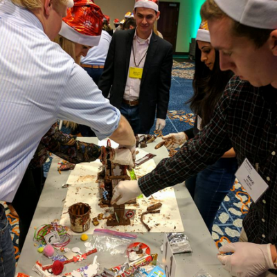 Team members wearing festive hats compete at a chocolate challenge during a holiday team building event. thumbnail