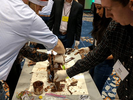 Team members wearing festive hats compete at a chocolate challenge during a holiday team building event.