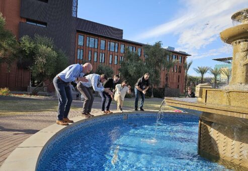Group of five team building participants crouched near a water fountain, preparing to take action during an outdoor team building activity.