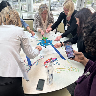 A group of women are gathered around a table, working together on a team building activity called 