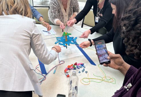 A group of women are gathered around a table, working together on a team building activity called 