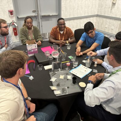 A group of professionals gather around a table, collaborating on assembling water filtration kits during a Clean Water Connection team building event. The team works together on this interactive project, learning about the global water crisis and the impact of providing clean water to communities in need. The activity fosters teamwork and raises awareness of clean water challenges around the world. thumbnail
