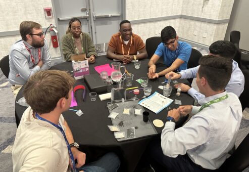 A group of professionals gather around a table, collaborating on assembling water filtration kits during a Clean Water Connection team building event. The team works together on this interactive project, learning about the global water crisis and the impact of providing clean water to communities in need. The activity fosters teamwork and raises awareness of clean water challenges around the world.