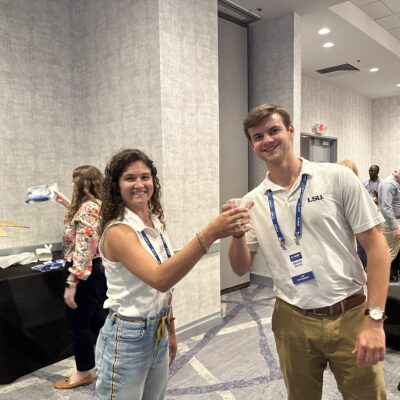 Two smiling participants at a Clean Water Connection event raise glasses of clean water, celebrating the successful assembly of a water filtration kit. The team building activity fosters teamwork and raises awareness about the importance of providing clean water to communities in need. thumbnail