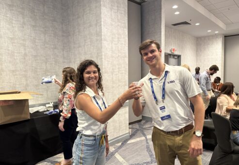 Two smiling participants at a Clean Water Connection event raise glasses of clean water, celebrating the successful assembly of a water filtration kit. The team building activity fosters teamwork and raises awareness about the importance of providing clean water to communities in need.