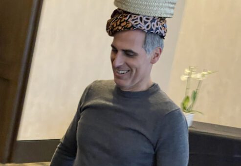 A smiling man participates in a water walk challenge by balancing a basket on his head during a Clean Water Connection team building event.