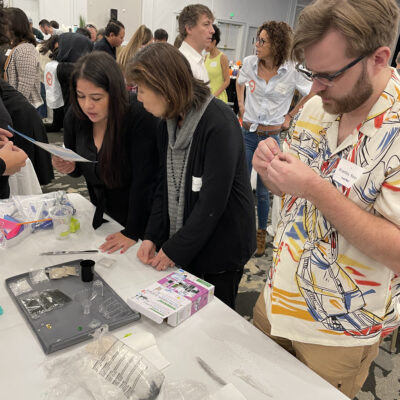 Participants at a Clean Water Connection team building event gather around a table, carefully reading instructions and assembling water filtration kits. The hands-on activity teaches them about water filtration technology and its importance in providing clean water to communities in need.