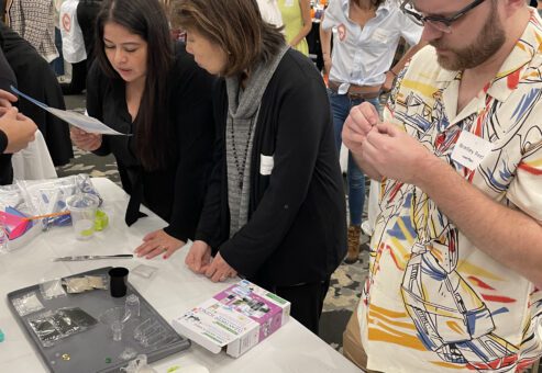 Participants at a Clean Water Connection team building event gather around a table, carefully reading instructions and assembling water filtration kits. The hands-on activity teaches them about water filtration technology and its importance in providing clean water to communities in need.