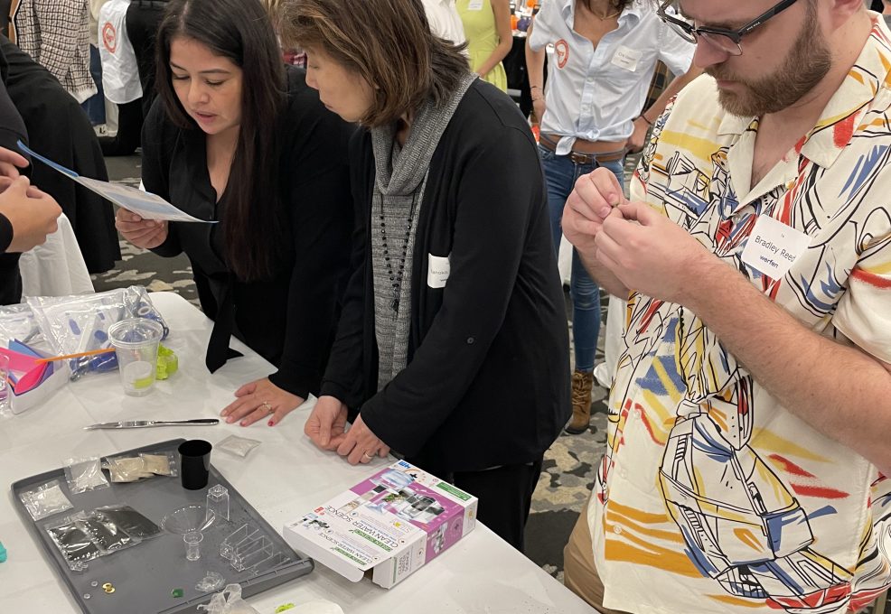 Participants at a Clean Water Connection team building event gather around a table, carefully reading instructions and assembling water filtration kits. The hands-on activity teaches them about water filtration technology and its importance in providing clean water to communities in need.