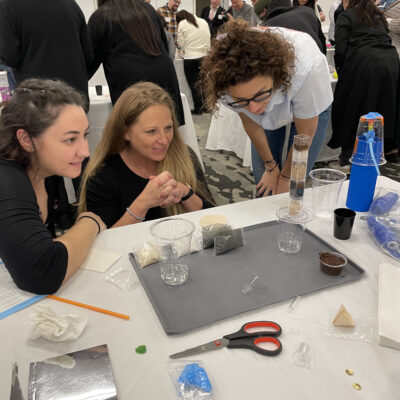 Three participants at a Clean Water Connection team building event closely observe their water filtration assembly in progress. The hands-on activity allows them to understand how filtration systems work and the importance of clean water access.