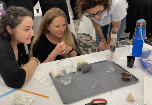 Three participants at a Clean Water Connection team building event closely observe their water filtration assembly in progress. The hands-on activity allows them to understand how filtration systems work and the importance of clean water access.
