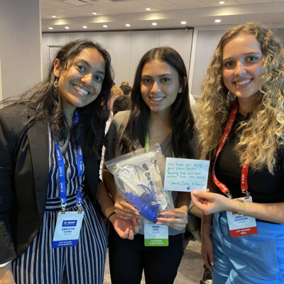 Three smiling women proudly display a completed water filtration kit and a handwritten note during a Clean Water Connection team building event. thumbnail