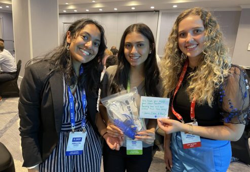 Three smiling women proudly display a completed water filtration kit and a handwritten note during a Clean Water Connection team building event.