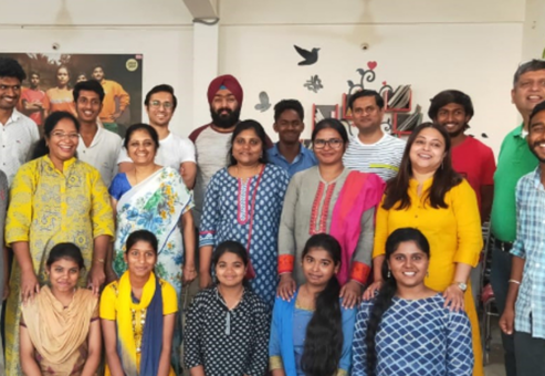 A group of men, women, and children from a rural community in India gather together for a group photo, smiling as they celebrate the donations they have received. The diverse group, dressed in colorful traditional and modern attire, reflects the joy and gratitude of the local community benefiting from the donation project.