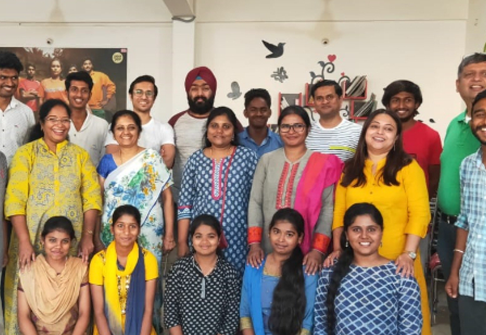 A group of men, women, and children from a rural community in India gather together for a group photo, smiling as they celebrate the donations they have received. The diverse group, dressed in colorful traditional and modern attire, reflects the joy and gratitude of the local community benefiting from the donation project.