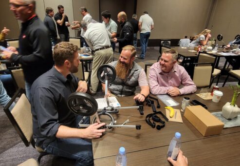 A group of three teammates collaborates enthusiastically to assemble a pet wheelchair during a team building event, working together to support animals in need.