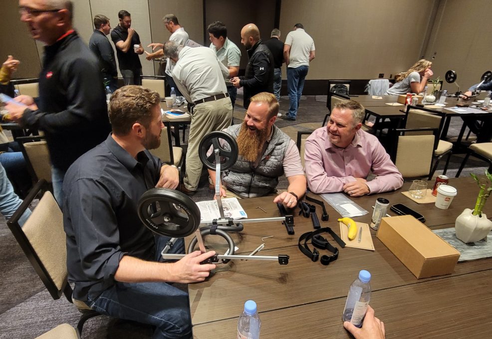 A group of three teammates collaborates enthusiastically to assemble a pet wheelchair during a team building event, working together to support animals in need.