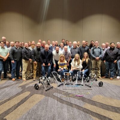 A large group of participants proudly standing together after successfully assembling pet wheelchairs during a team building event, showcasing their completed projects in front of them. The focus is on teamwork and making a meaningful impact on animal welfare. thumbnail